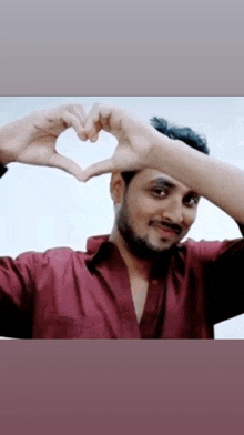 a man in a maroon shirt making a heart shape with his hands