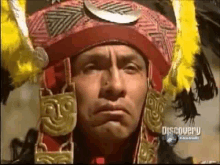 a man wearing a red hat and a yellow feathered headdress is making a funny face .