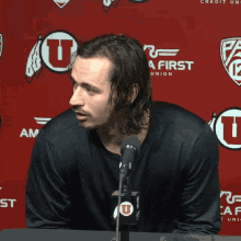 a man stands in front of a microphone in front of a red backdrop that says rica first edit union