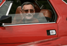 a man wearing sunglasses is smiling while driving a red car