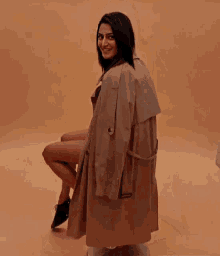 a woman in a trench coat is sitting on a stool .