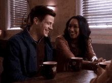 a man and a woman are sitting at a table with cups of coffee and smiling .