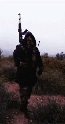 a man in a hooded jacket is holding a gun in a field