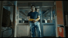 a man in a black shirt and blue jeans is standing on a train with a yellow bandage on his arm .