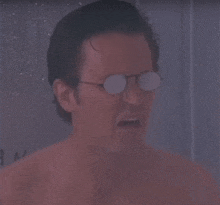 a shirtless man wearing glasses is taking a shower in a bathroom .