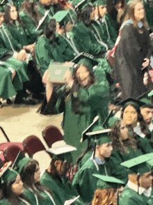 a group of graduates in green gowns and caps are sitting in rows