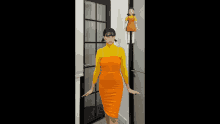 a woman in an orange dress and yellow turtleneck is standing next to a doll .