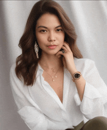 a woman wearing a white shirt and a watch looks at the camera