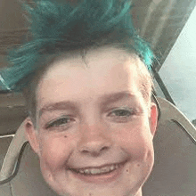 a young boy with blue hair is sitting in a car seat smiling .