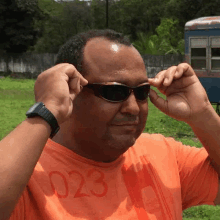 a man wearing an orange shirt with the number 023 on it is adjusting his sunglasses .