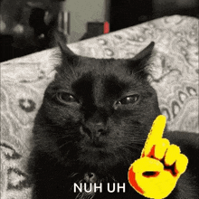 a black cat is laying on a bed with a yellow finger pointing up and the words nuh uh .