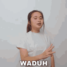 a girl in a white shirt is making a funny face and the word waduh is on the bottom of her shirt