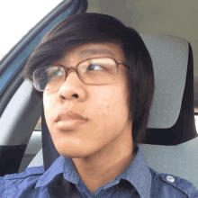 a young man wearing glasses and a blue shirt is sitting in the driver 's seat of a car