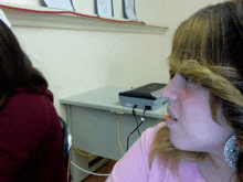 a woman in a pink shirt is sitting at a desk with a small device on it that says ' ethernet ' on it