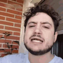 a man with curly hair and a beard is making a funny face in front of a brick wall .