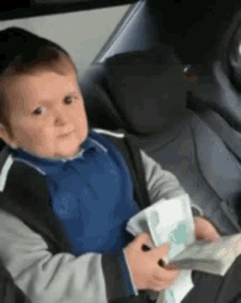 a young boy is sitting in the back seat of a car holding a stack of money and a book .