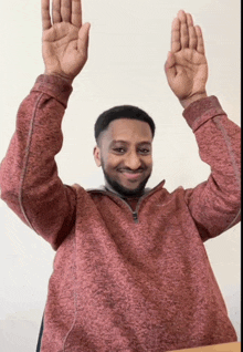 a man wearing a maroon sweater is raising his hands in the air