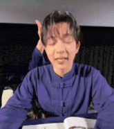 a man in a purple shirt is sitting at a table with his eyes closed and making a funny face .