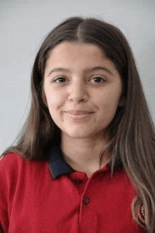 a young girl is wearing a red polo shirt and smiling .