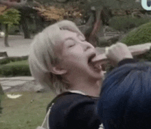 a man with white hair is eating ice cream in a park while another man watches .