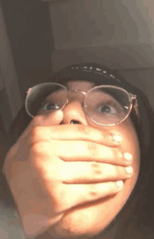 a person wearing glasses covering their mouth with their hands