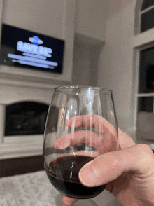 a person is holding a glass of red wine in front of a tv screen that says save me