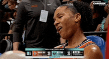 a woman is sitting in the stands watching a basketball game with a scoreboard behind her .