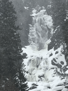 a waterfall is surrounded by snow covered trees