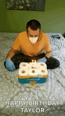 a man wearing a mask is sitting on a bed with a birthday cake made out of toilet paper .