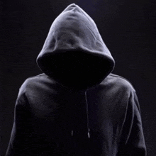 a man in a hooded sweatshirt is standing in the dark without a face .