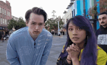 a woman with purple hair is standing next to a man wearing a blue shirt that says fools air warm wings