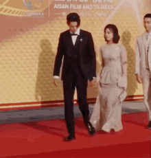 a man in a tuxedo and a woman in a dress walk on a red carpet at an asian film and tv week event