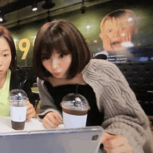 a woman sits at a table with a cup of coffee in front of a sign that says 9