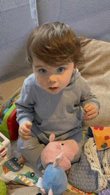 a baby is sitting on the floor with a stuffed animal and a toy that says ' peppa pig ' on it