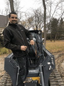 a man in a black jacket stands next to a john deere tractor