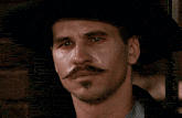 a man with a mustache wearing a cowboy hat looks at the camera