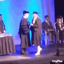 a woman in a graduation cap and gown shakes hands with a man in a graduation cap and gown .