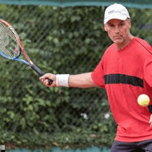 a man in a red shirt is holding a tennis racquet and a ball .