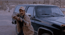 a man holding a gun in front of a black truck with a hat that says ' texas ' on it