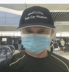 a man wearing a saab car museum hat and a face mask