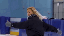 a woman in a black jacket is standing on a ice rink with a tv logo on the wall behind her