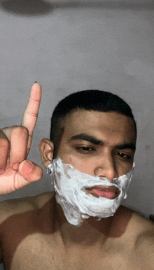 a shirtless man with shaving foam on his face giving the middle finger