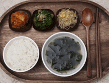 a wooden tray with bowls of food including rice and a bowl of soup