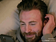a man with a beard is laying on a bed looking at a cell phone .