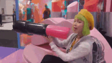 a woman with green hair is sitting on a pink couch holding a pink lipstick cannon .