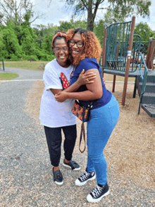 two women hugging in front of a playground with one wearing a minnie mouse shirt