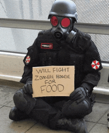 a man in a gas mask sits on the ground holding a sign that says will fight zombie horde for food