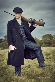 a man in a suit is holding a gun in a field and pointing at it .