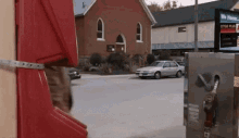 a white car is being pumped into a gas pump at a gas station with a red building in the background ..