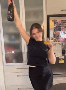 a woman is holding a bottle of wine and a glass of wine in front of a refrigerator with the letter n on the door